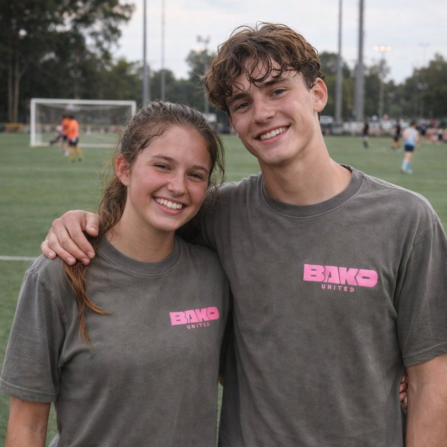 Two people wearing gray t-shirts with a Bako United logo on a sports field.